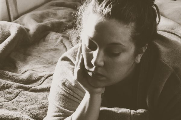 Photo of a young woman laying on a bed with her head resting on her hand. HOLLY LAY via FLICKR CC BY 2.0