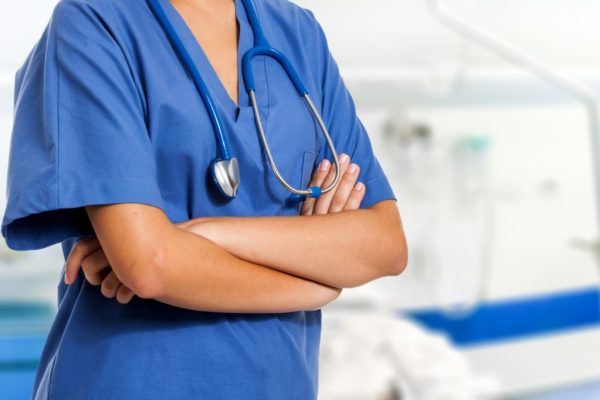 A nurse in blue scrubs against a blurred background